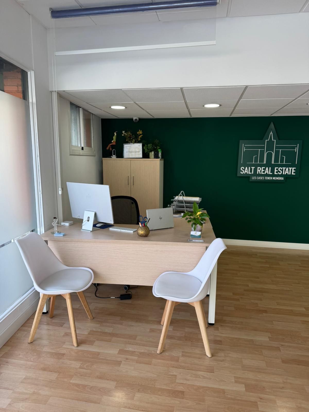 Interior de oficina con escritorio y sillas; pared con acento verde oscuro, logotipo de Salt Real Estate.