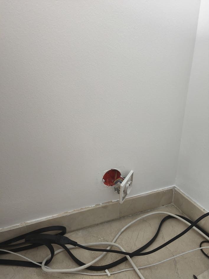 Prise murale ouverte avec des fils rouges dénudés près de la plinthe et des câbles qui traînent au sol