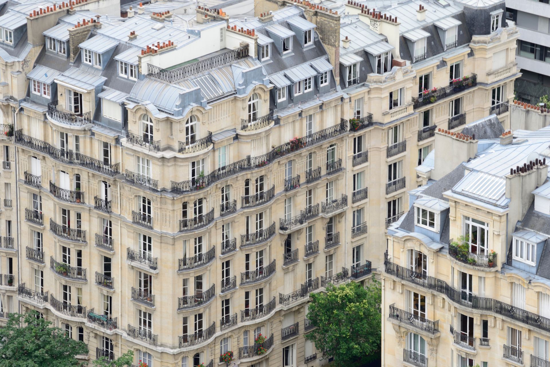 Vue aérienne d'immeubles parisiens beiges avec toits mansardés blancs et balcons.