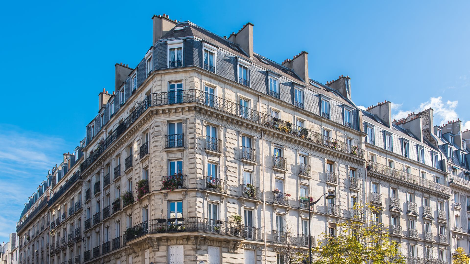 Immeuble d'appartements blanc de style parisien avec balcons sous un ciel bleu éclatant.