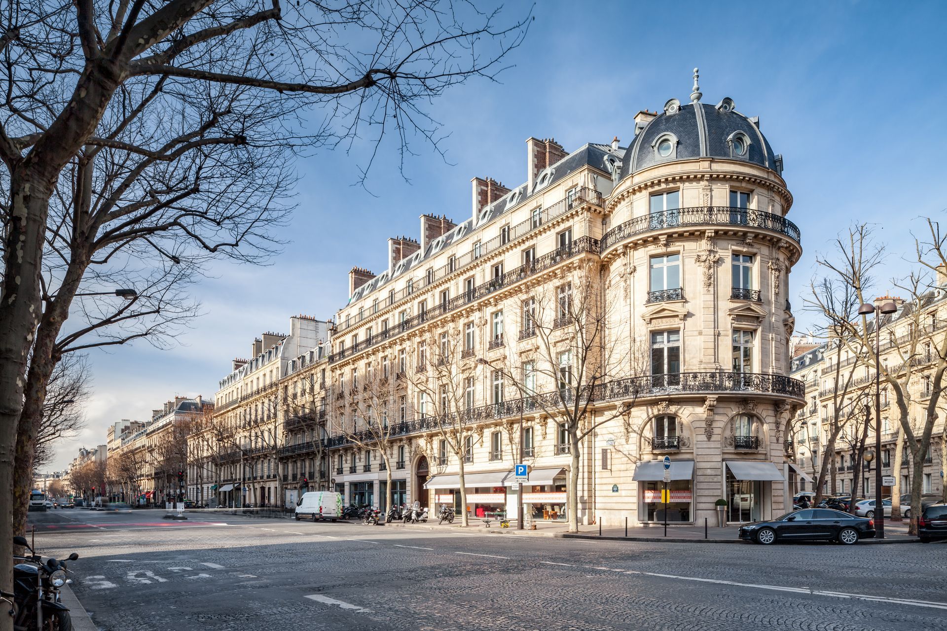 Élégant immeuble parisien couleur crème, situé dans une rue calme et arborée sous un ciel d'un bleu limpide.