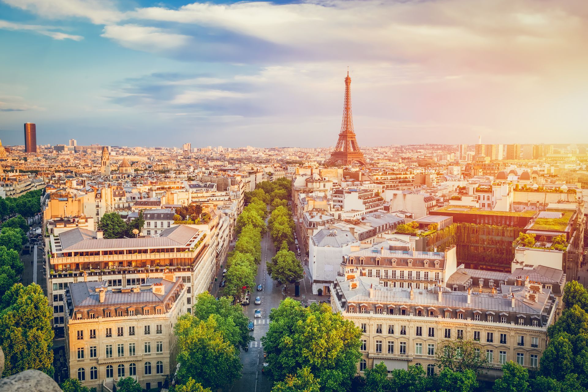 Vue de Paris avec la Tour Eiffel dominant les avenues bordées d'arbres au coucher du soleil.