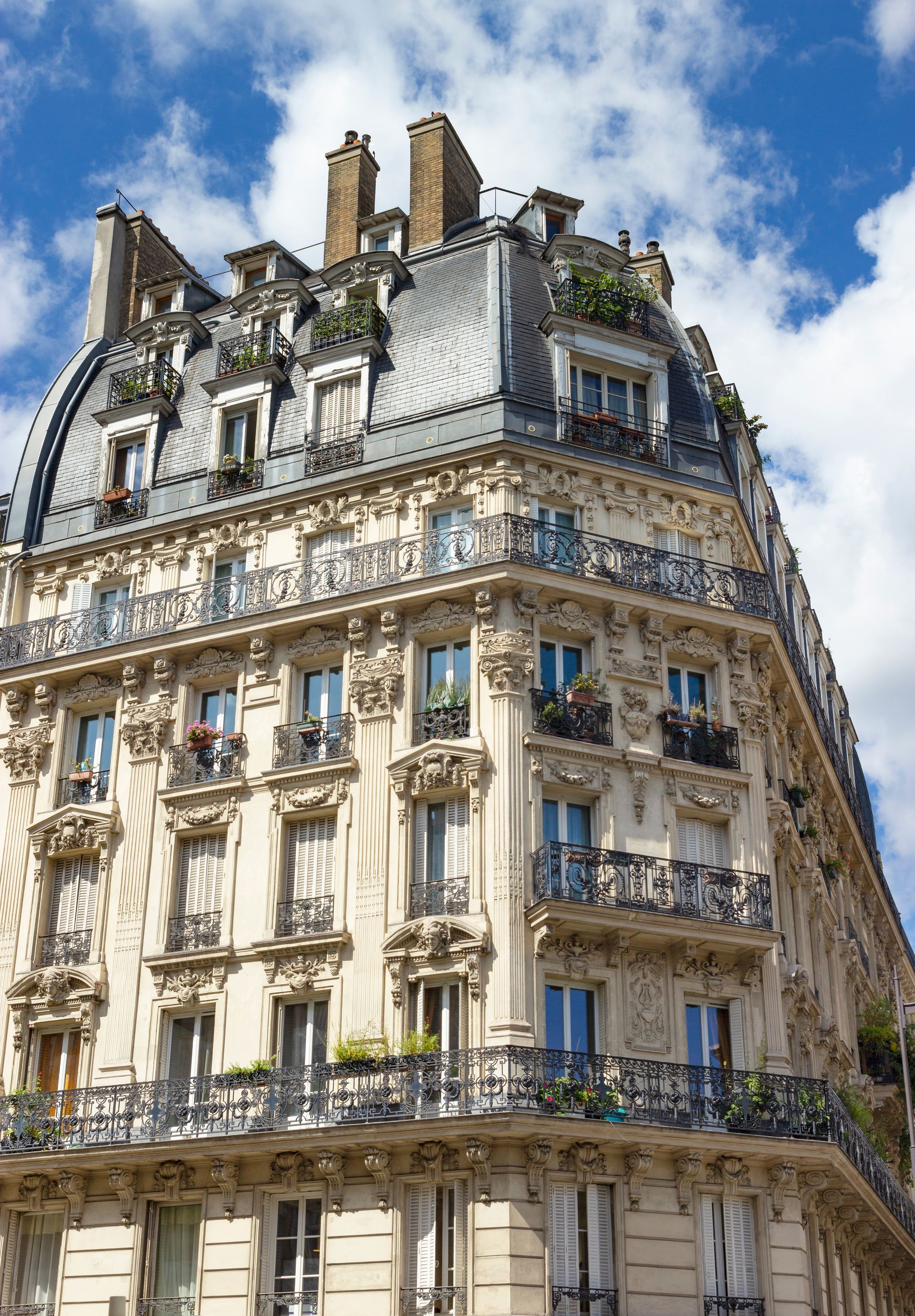 Immeuble parisien orné, façade crème et toit mansardé se détachant sur un ciel bleu