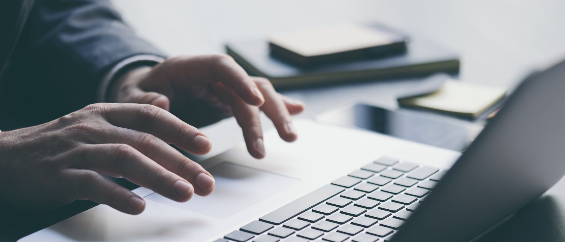 Une personne tape sur le clavier d'un ordinateur portable, un carnet et un téléphone à proximité.