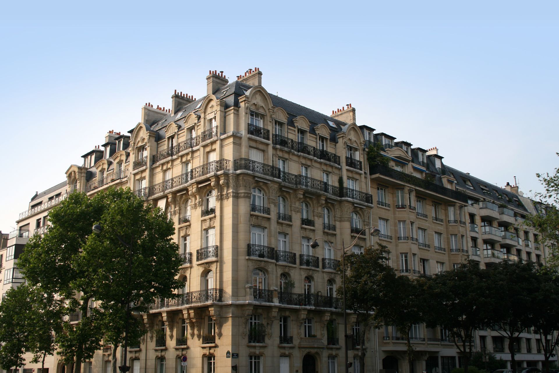 Immeuble d'appartements beige de style haussmannien avec balcons ornés et arbres bordant la rue.