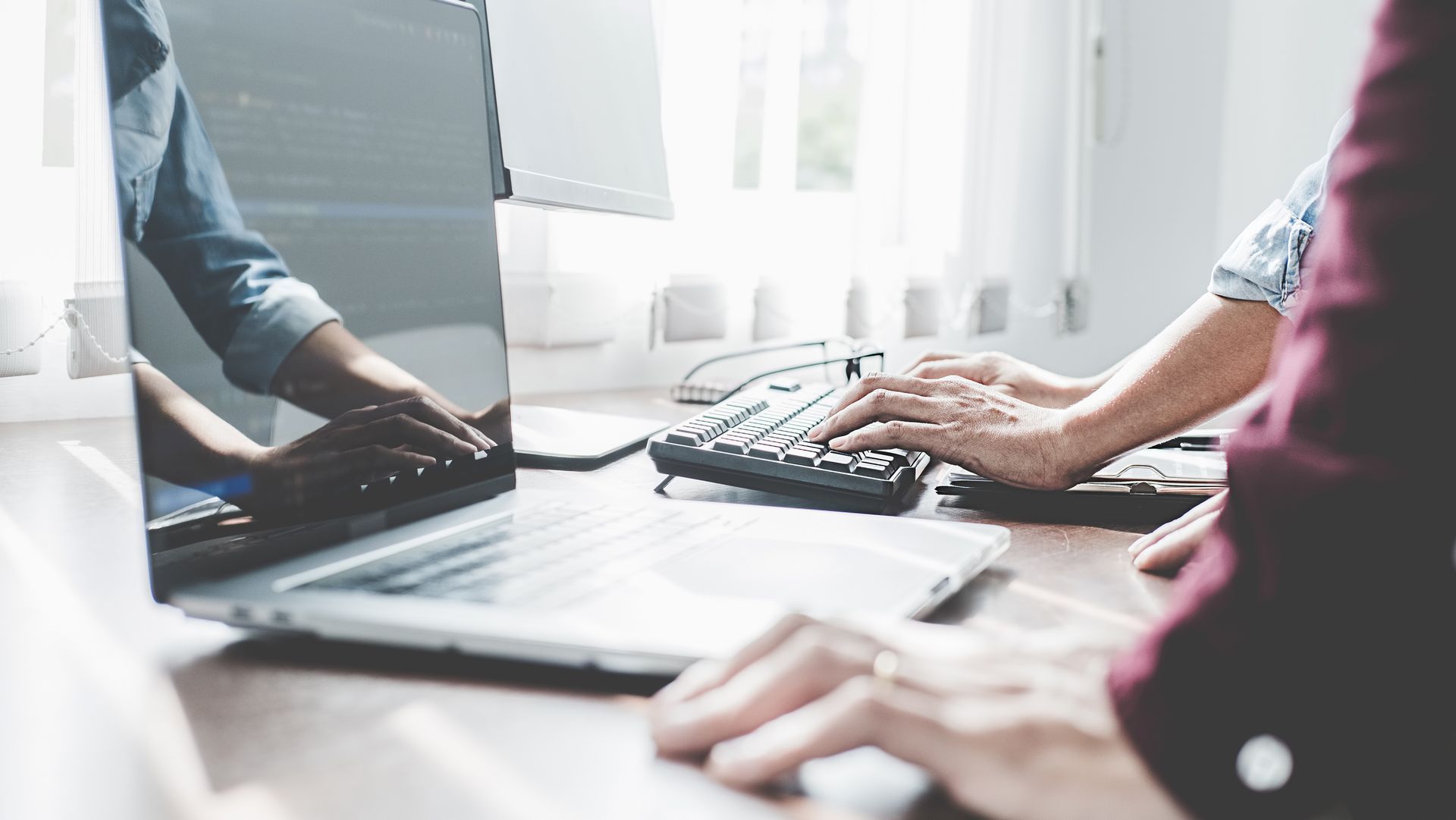 Des personnes tapant sur des ordinateurs portables et un clavier de bureau autour d'une table de conférence lumineuse.