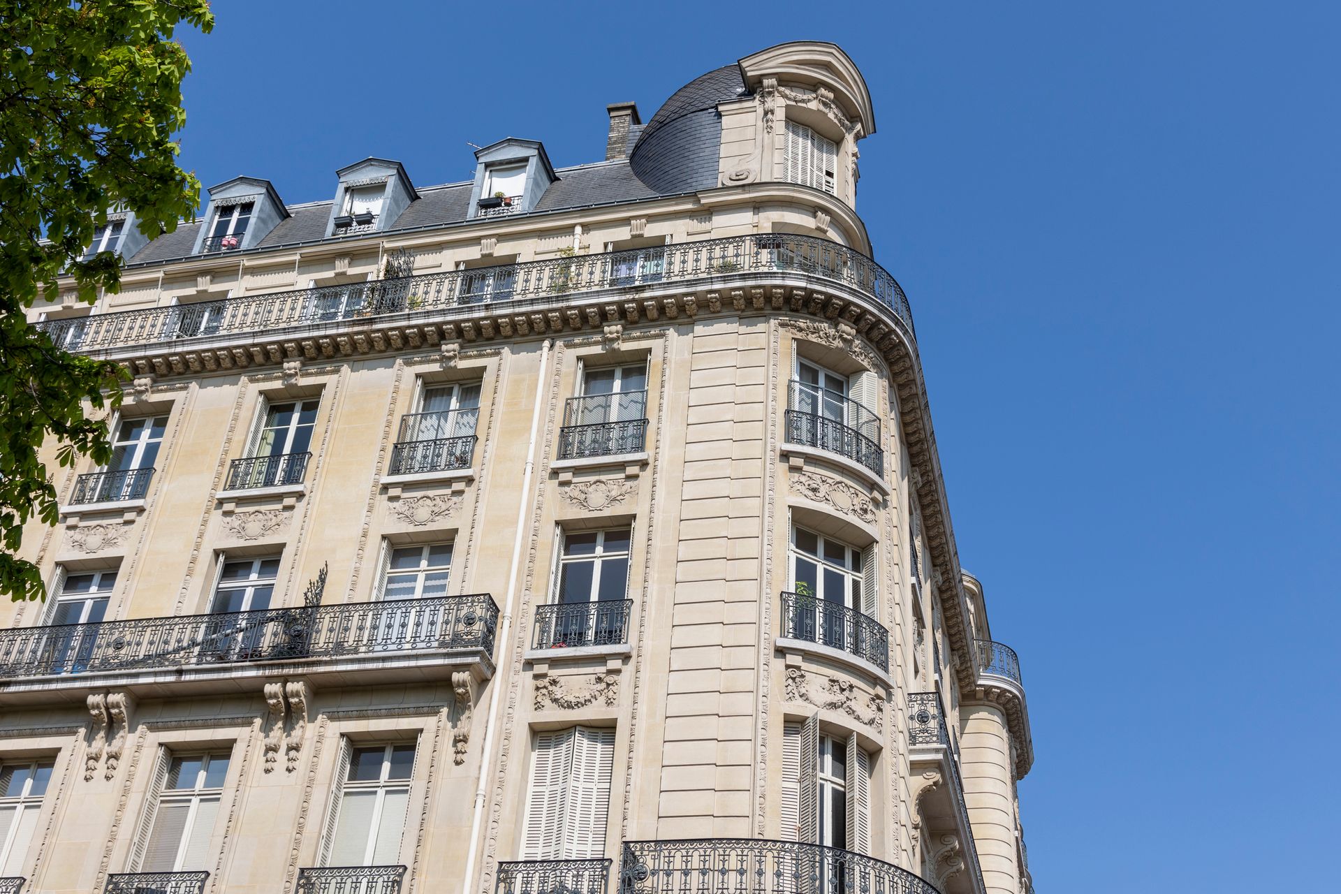 Immeuble parisien orné, couleur crème, avec balcons se détachant sur un ciel bleu clair.