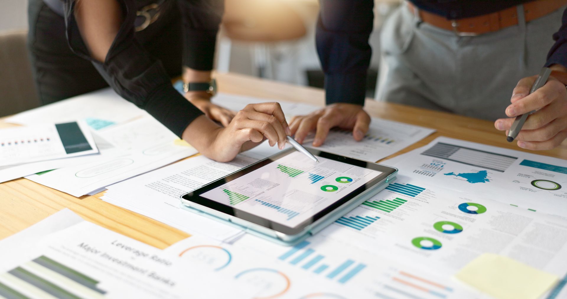 Des personnes consultent des graphiques imprimés et une tablette affichant des graphiques analytiques sur un bureau.
