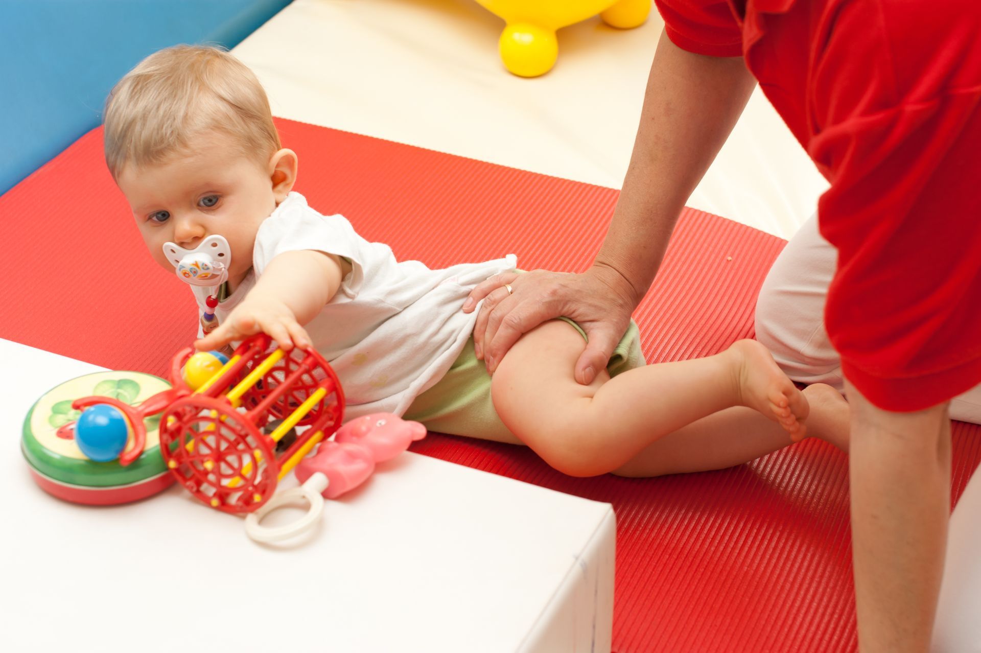 Ein Baby mit Schnuller spielt mit einem Spielzeug auf dem Boden.