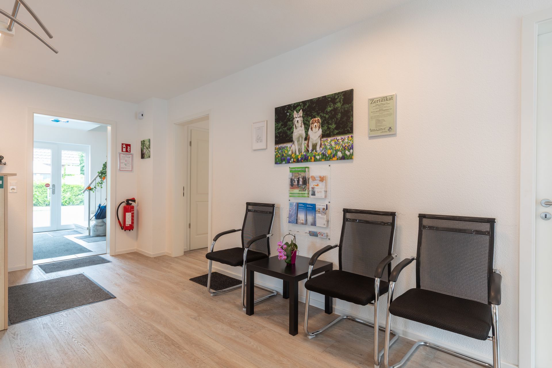 Ein Wartezimmer mit Stühlen, einem Tisch und einem Bild an der Wand.