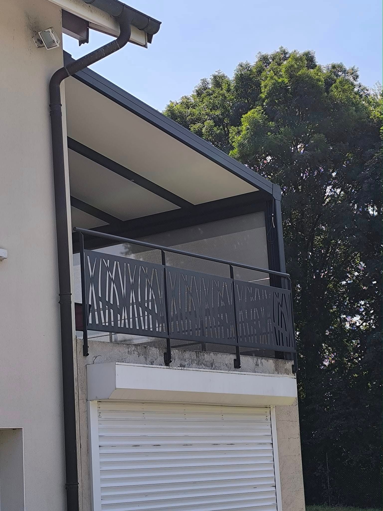 Une terrasse recouverte d'une pergola avec un garde-corps décoratif en alu gris foncé.