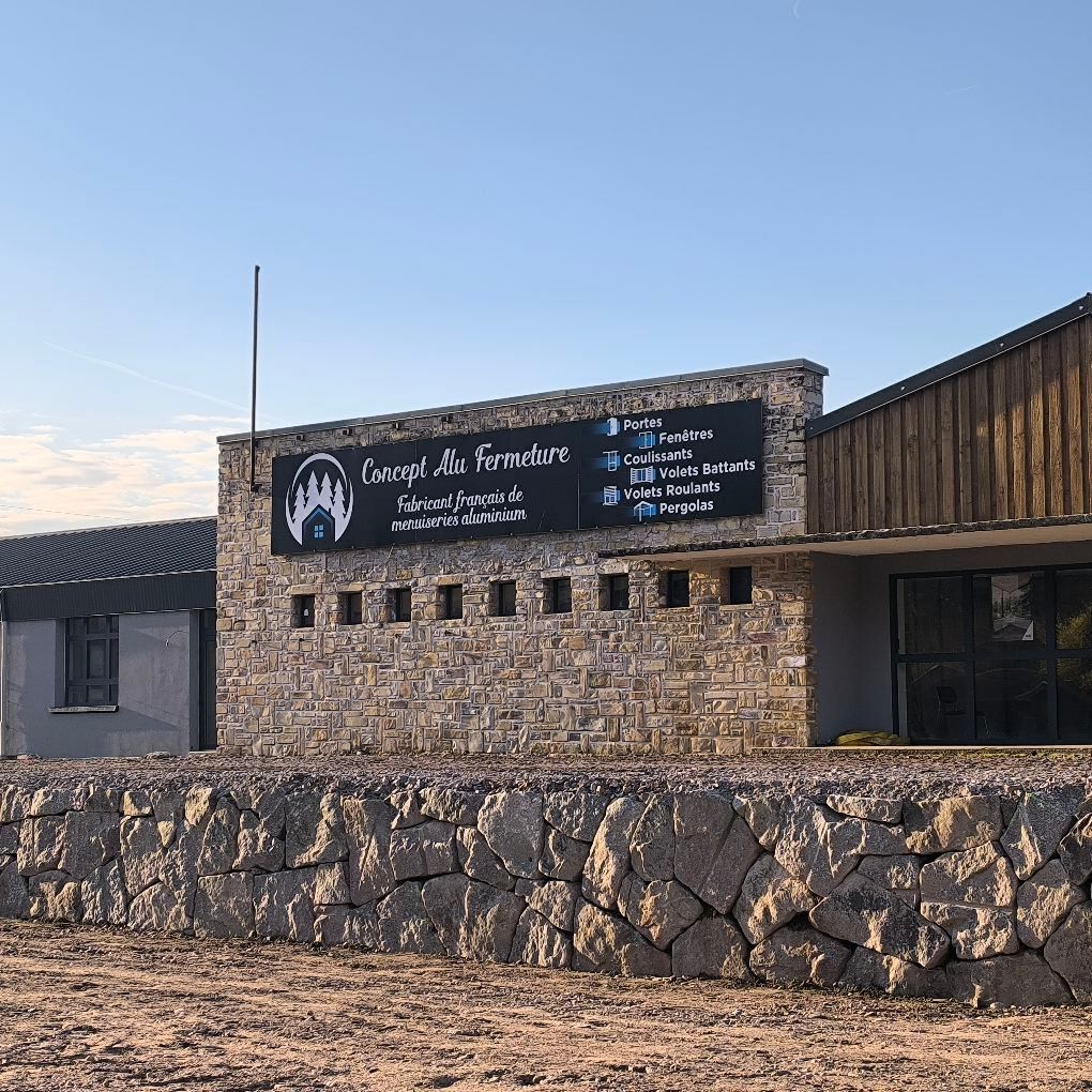 Un bâtiment en pierre arborant une enseigne noire de l'entreprise Concept Alu Fermeture.