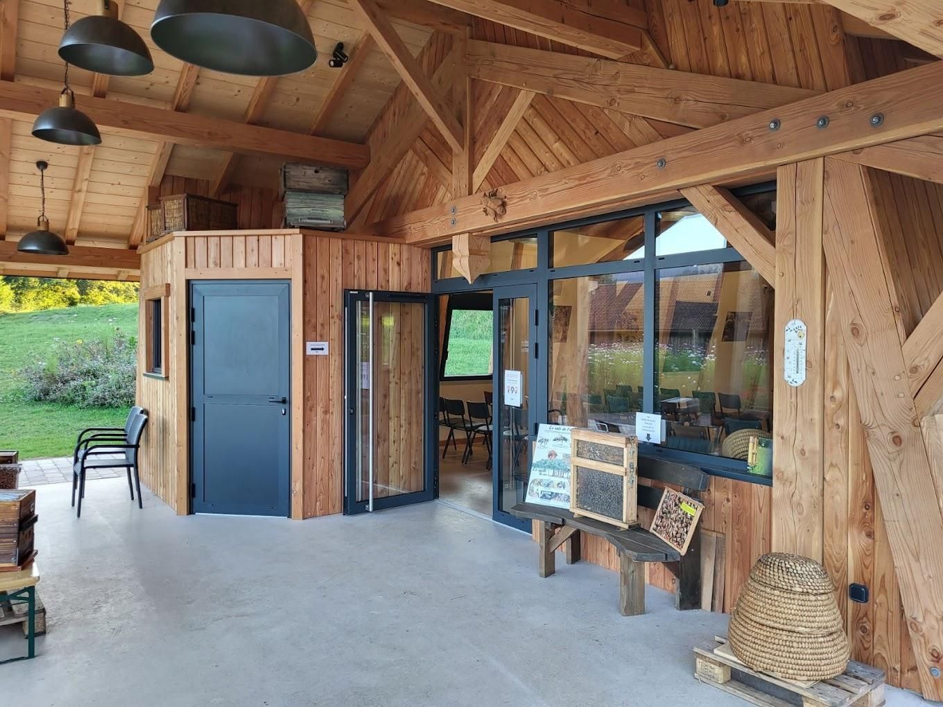 Un pavillon en bois avec des portes en aluminium, de grandes fenêtres, des suspensions lumineuses, des sièges extérieurs et une ruche en paille.