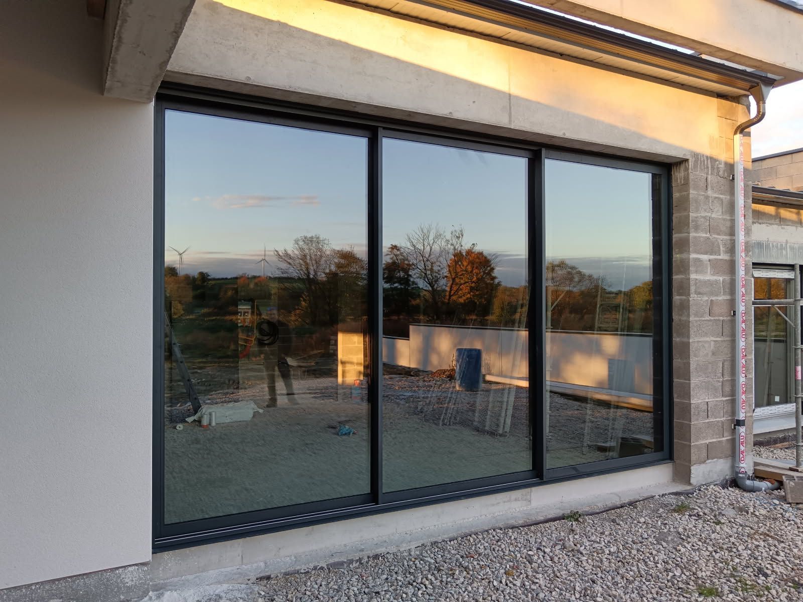 Grandes portes coulissantes en verre à trois vantaux et cadre noir en aluminium, reflétant un paysage extérieur.