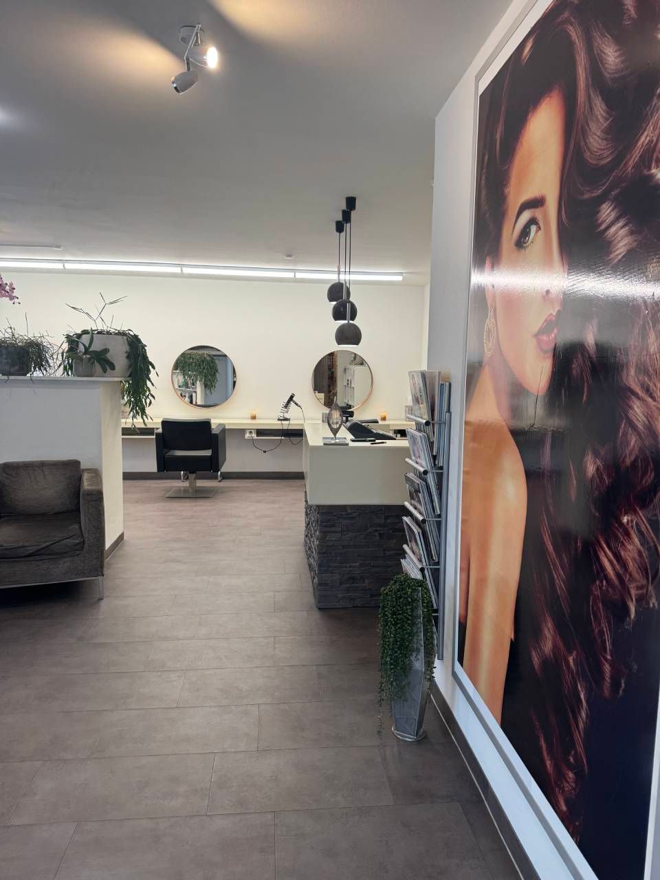 Interieur eines Friseursalons mit Spiegeln, Frisierplätzen und einem grossen Poster einer Frau mit gestylten Haaren.
