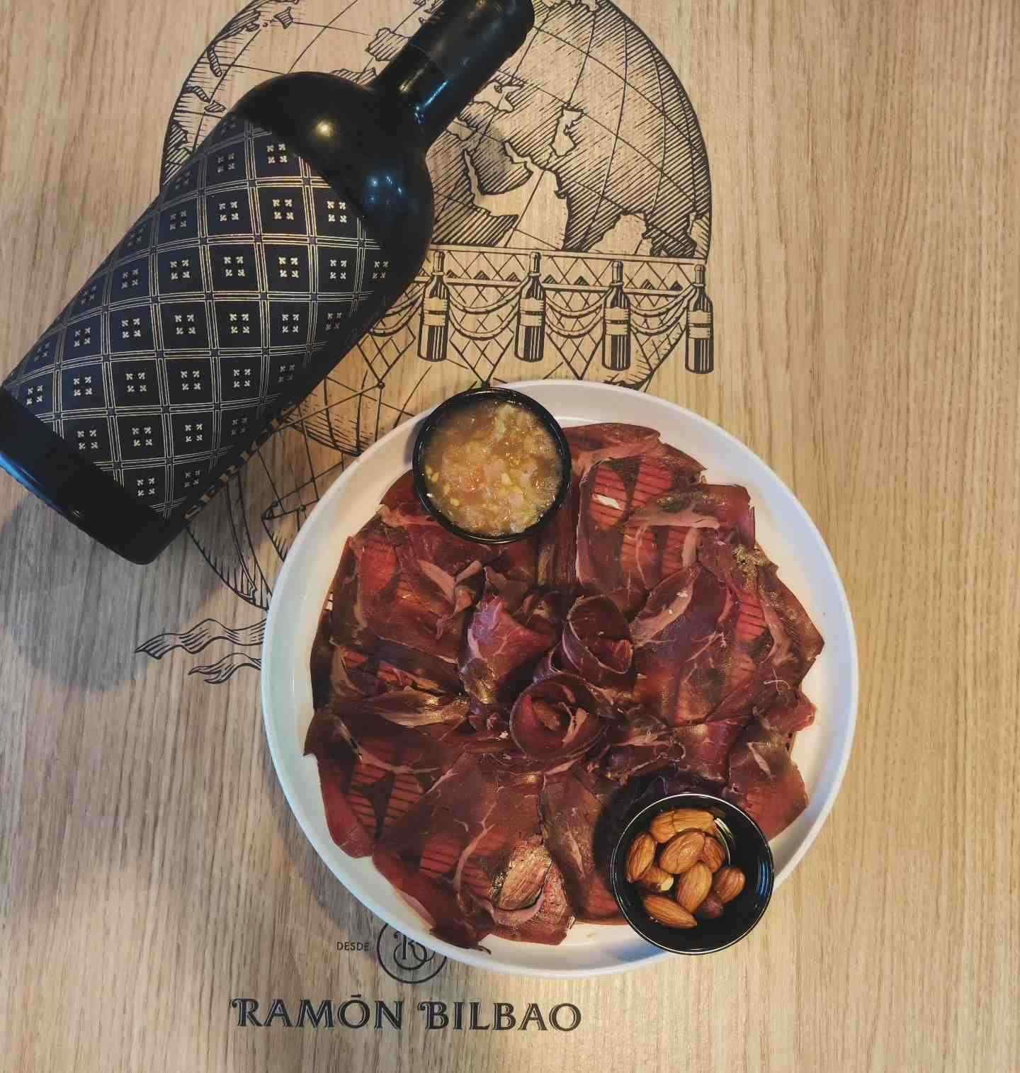 Botella de vino, plato de carne con almendras y salsa y un mapa de fondo.