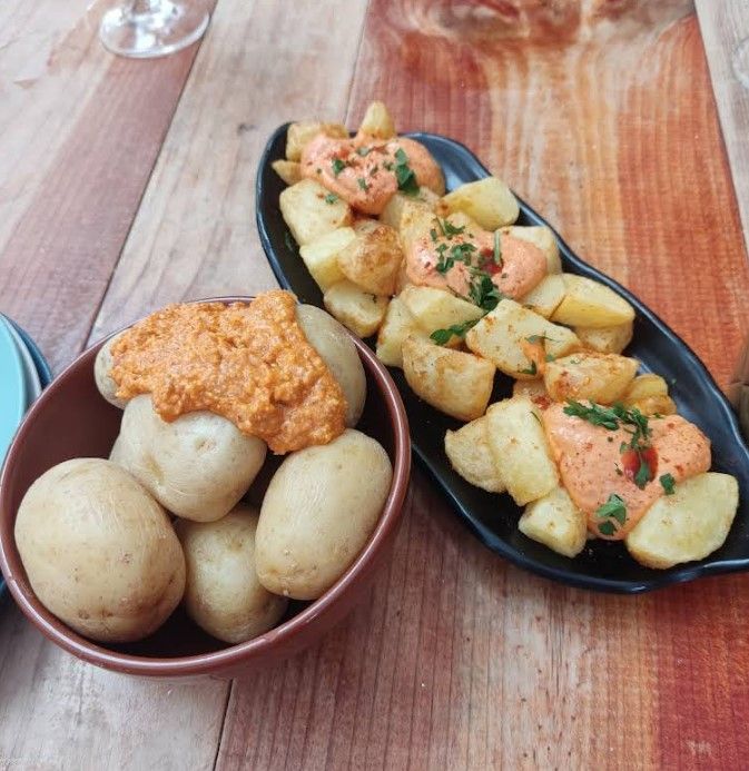 Patatas bravas y patatas arrugadas con salsa picante sobre una tabla de madera.