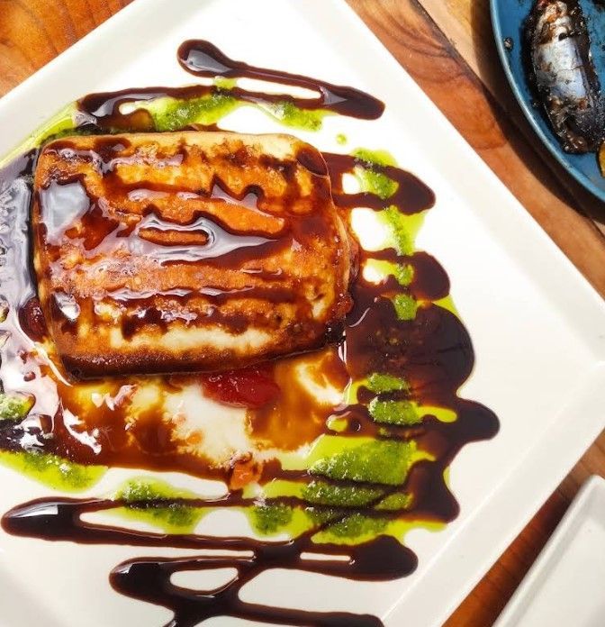 Queso frito con salsas marrón y verde en un plato blanco.