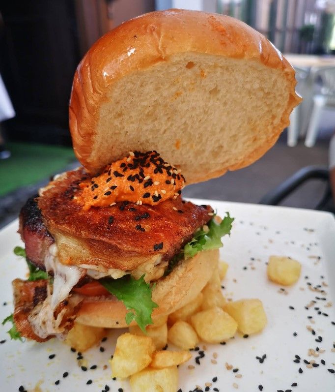 Hamburguesa en un plato blanco con patatas fritas y semillas de sésamo. El pan superior está levantado.
