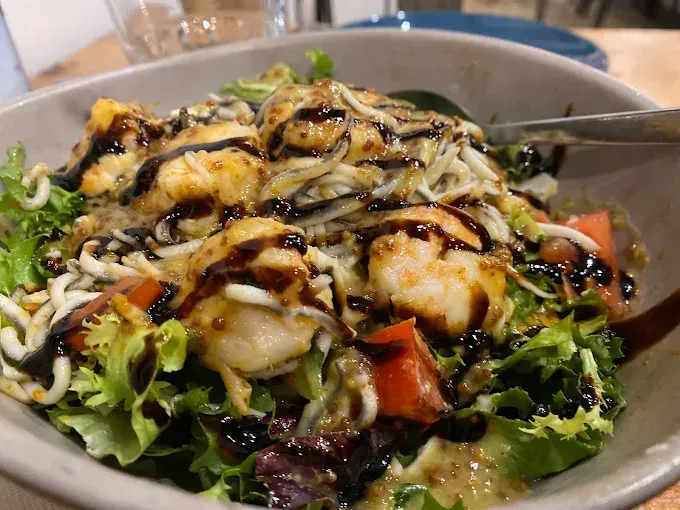 Ensaladera con verduras de hoja verde, tomates y mariscos, rociada con glaseado balsámico.