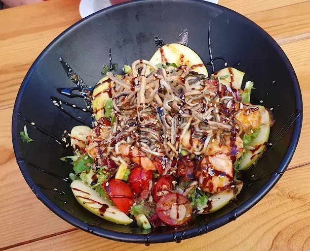 Tazón de ensalada negra con tomates, rodajas de manzana, aguacate, brotes y aderezo.
