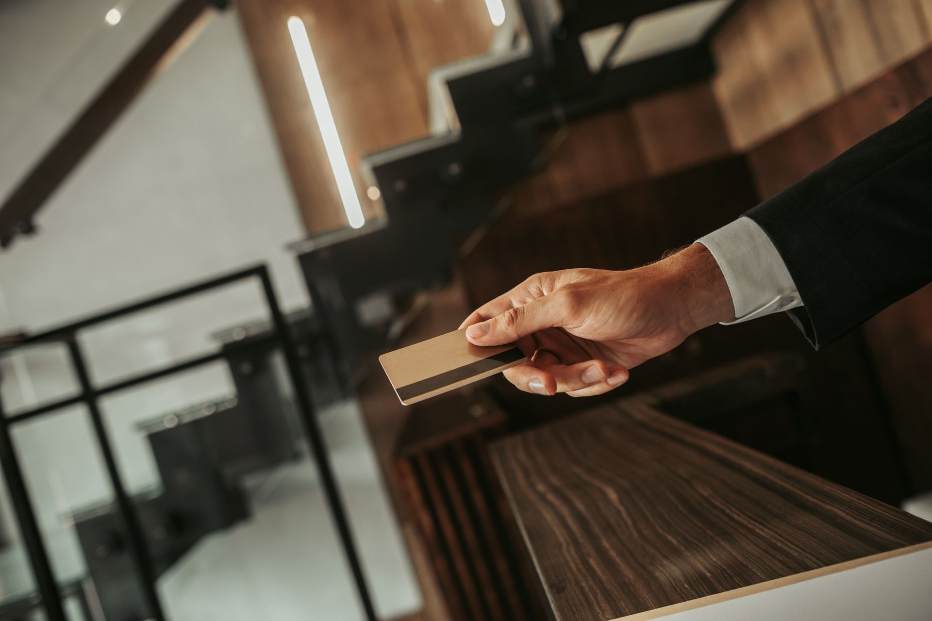 Persona de traje sosteniendo una tarjeta sobre un mostrador de madera en un entorno de oficina.