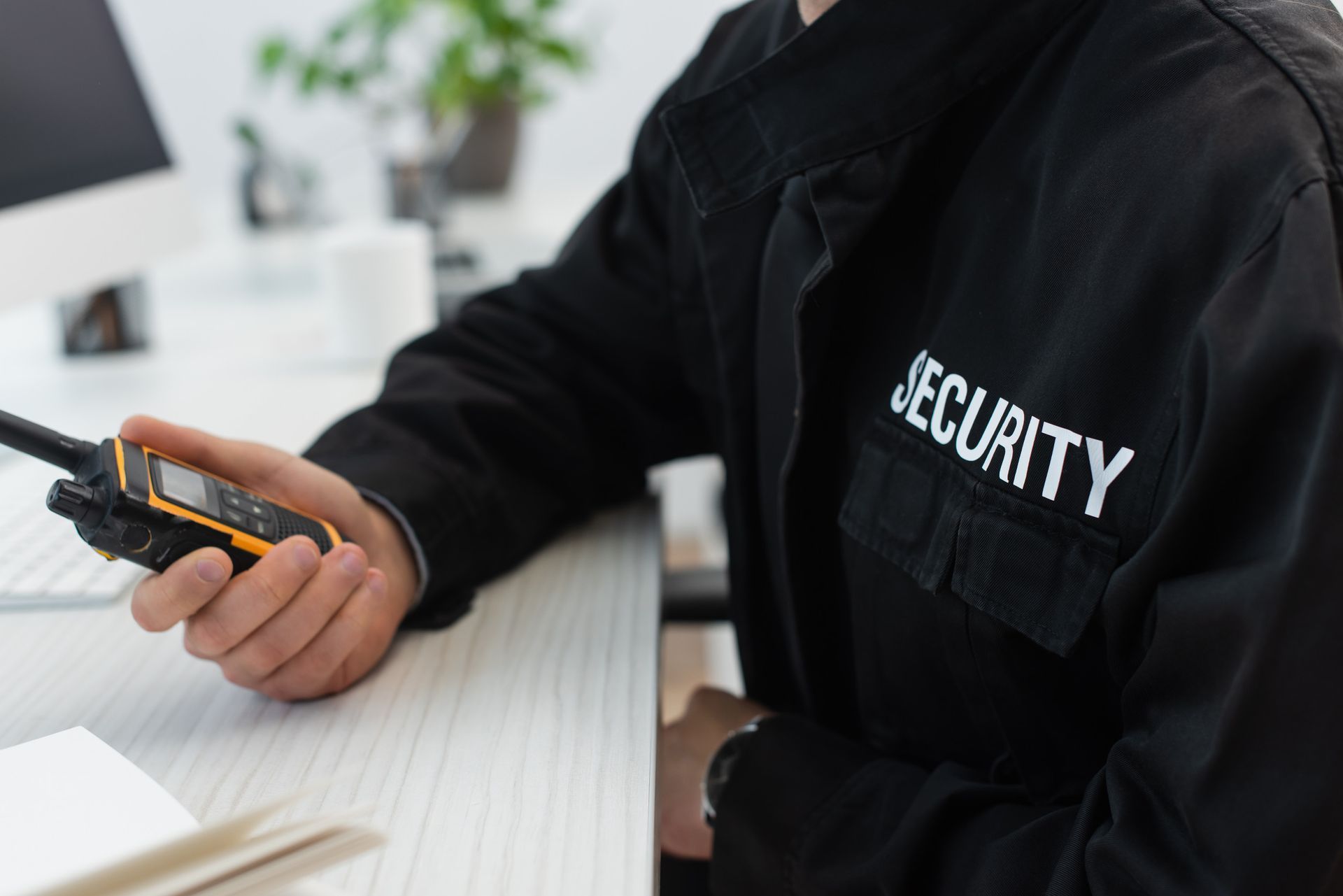 Guardia de seguridad con uniforme negro sosteniendo un walkie-talkie, sentado en un escritorio.