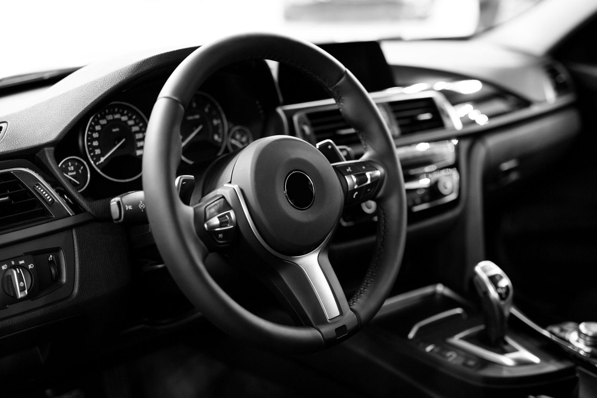 Interior en blanco y negro de un coche. Volante, salpicadero, palanca de cambios y otros controles visibles.