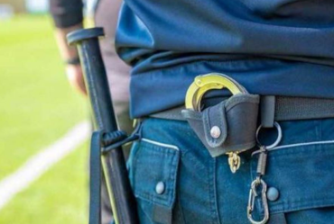 Cinturón de servicio de un oficial de policía con porra, esposas y otros equipos, sobre un campo verde borroso.