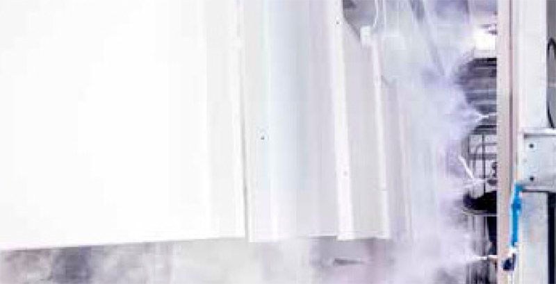 Paneles blancos rociados con una niebla en un entorno industrial. El vapor impregna el aire alrededor de los objetos.