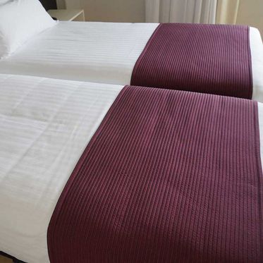 Dos camas individuales con sábanas blancas y caminos de cama color burdeos en un dormitorio.