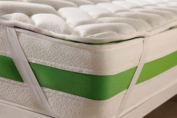 Primer plano de un colchón con una cubierta acolchada blanca, una banda decorativa verde y correas elásticas para asegurarlo al colchón.
