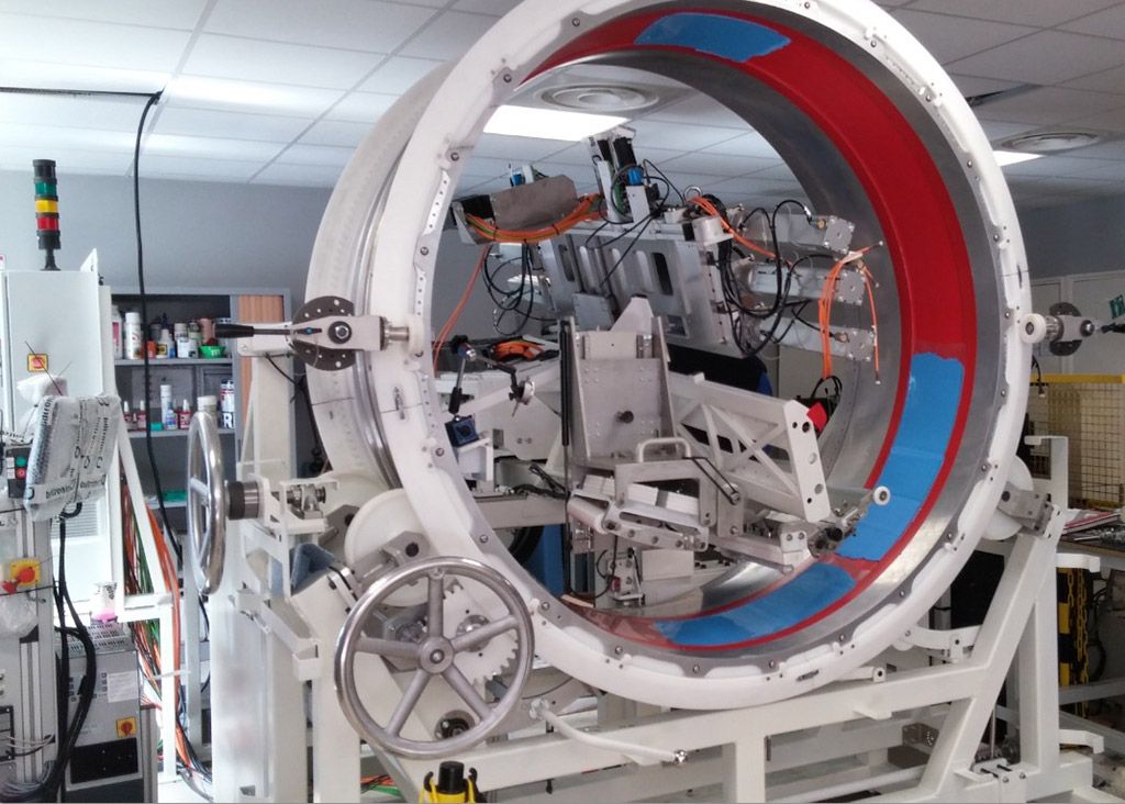 Grande machine blanche à anneau rotatif, contenant des sections bleues et rouges, dans un atelier.