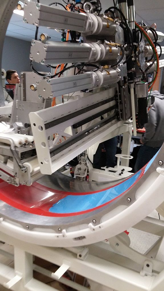 Bras robotisé enveloppant une pièce en plastique incurvée et multicolore dans un environnement d'usine.