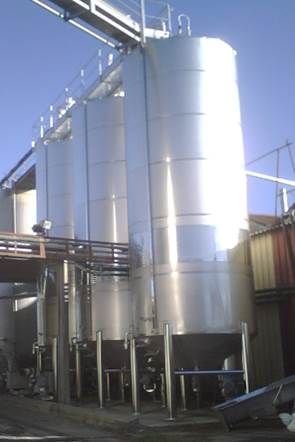 Trois grandes cuves cylindriques en acier inoxydable à l'extérieur sous un ciel bleu éclatant.