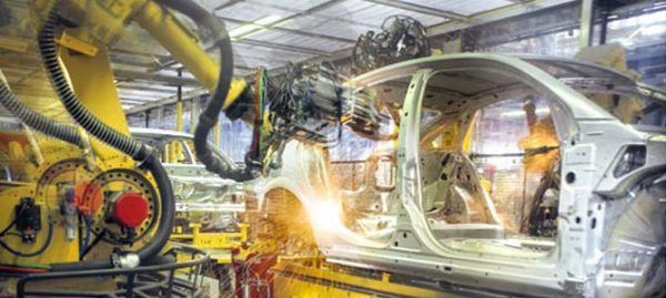 Des bras robotisés soudent un châssis de voiture dans une usine automobile.