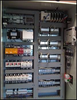 Panneau de commande électrique avec divers composants, fils et disjoncteurs dans un boîtier métallique gris.