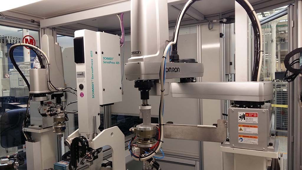 Bras robotisés assemblant des pièces dans une usine, avec plusieurs machines et équipements visibles.