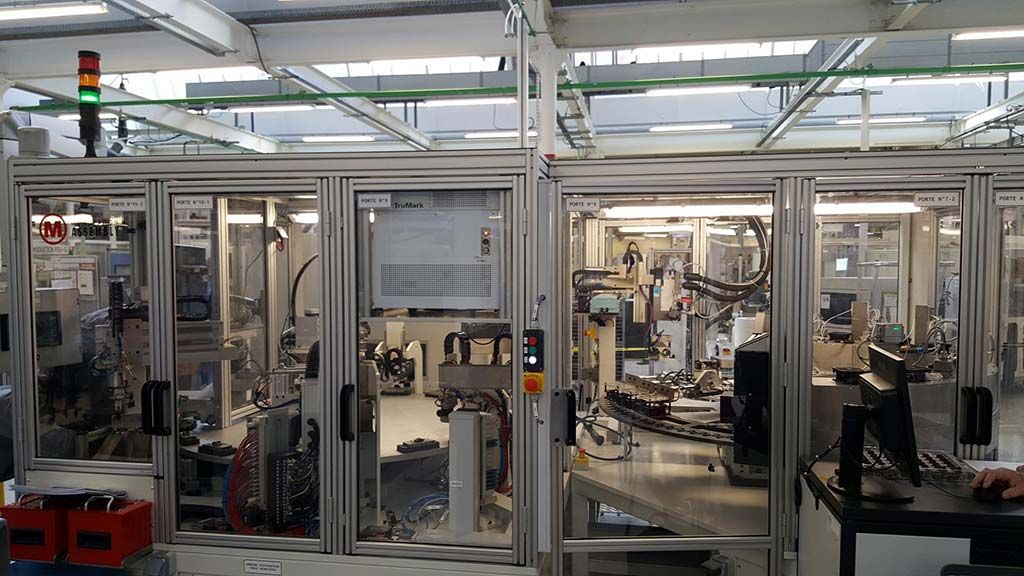 Chaîne de montage automatisée derrière des portes vitrées, avec des machines et un feu de circulation indiquant l'état dans une usine.