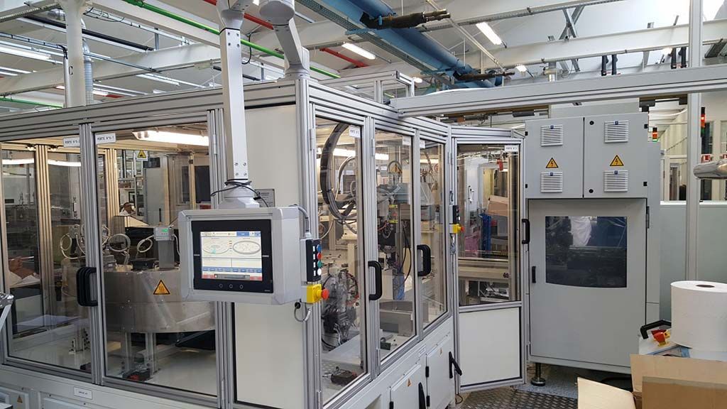 Machine industrielle automatisée en configuration usine, avec écran tactile et enceinte de sécurité.