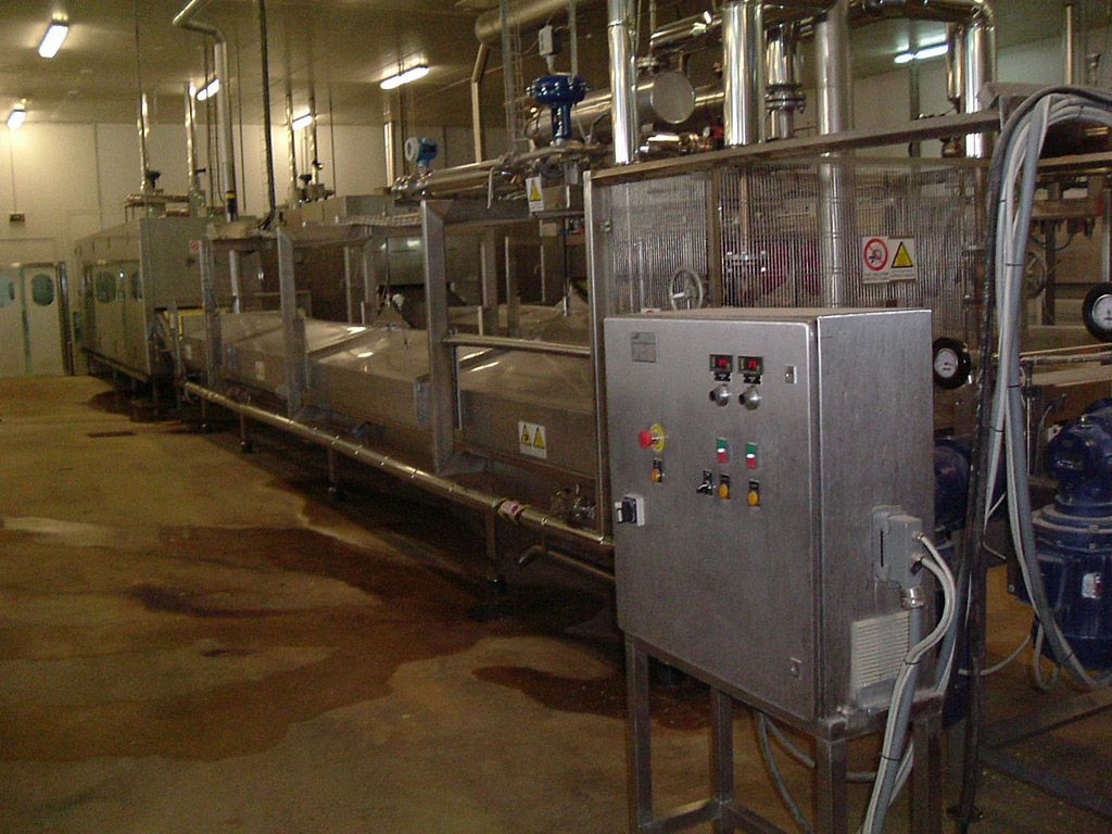 Machine industrielle de transformation alimentaire en configuration usine. En acier inoxydable, longue et rectangulaire. Panneau de commande visible.