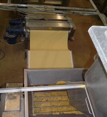 Machine à pâtes extrudant une feuille de pâte jaune dans un bac en acier inoxydable.