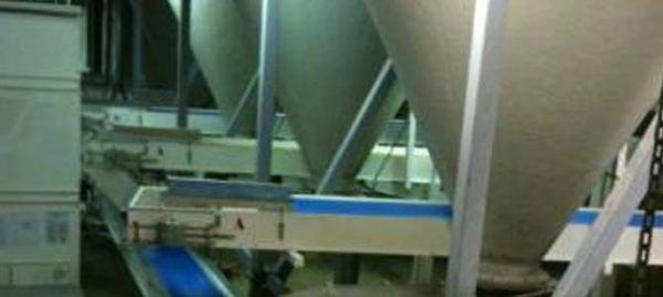 Machines dans une usine ; grands conteneurs de stockage cylindriques sur des bandes transporteuses.