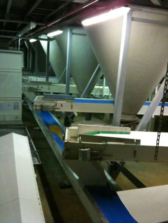 Intérieur industriel avec silos, bandes transporteuses et éclairage zénithal.