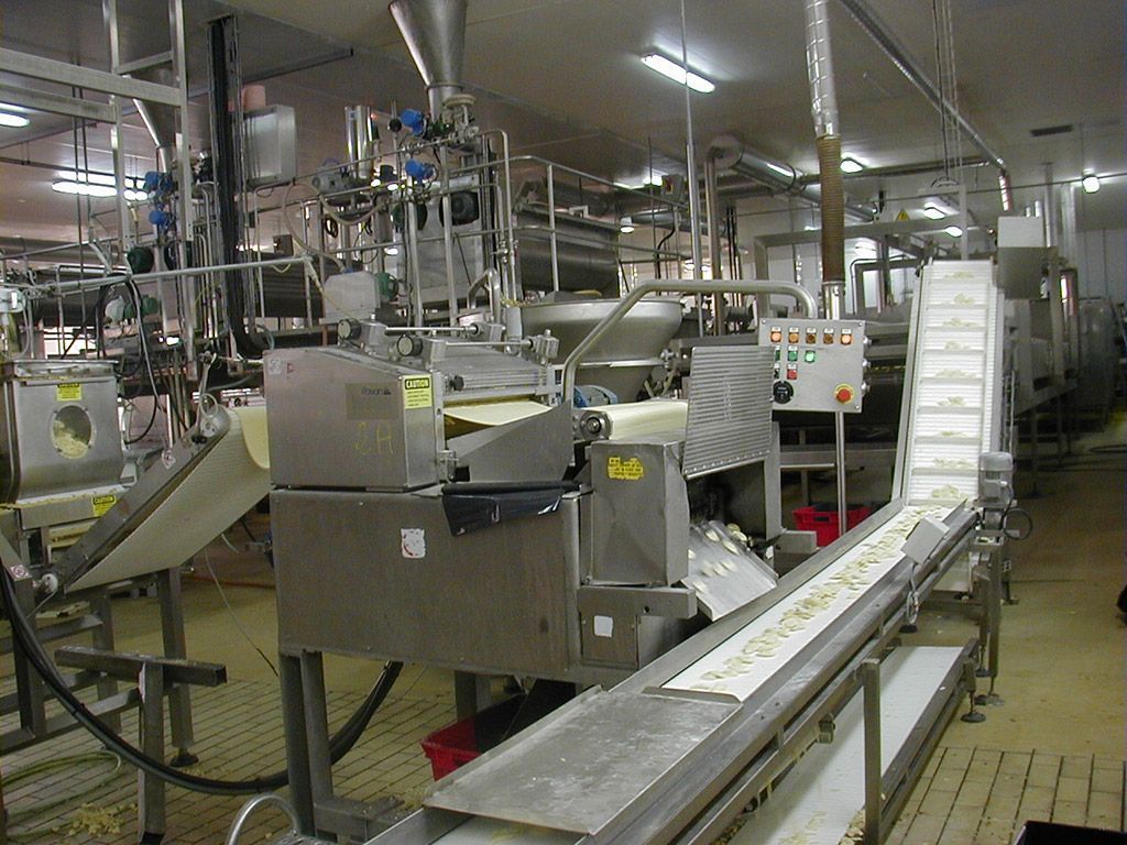 Équipement de transformation alimentaire industrielle en usine, avec convoyeurs, machines et panneau de commande.