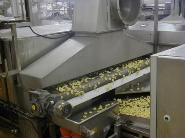 Un tapis roulant dans une usine de transformation alimentaire transporte de petits aliments jaunes.