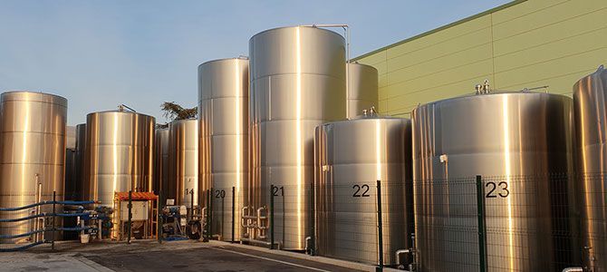 Cuves cylindriques en acier inoxydable dans une cave, numérotées 22 et 23, baignées de soleil.