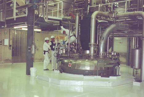 Trois ouvriers en costumes blancs examinent un grand récipient de mélange industriel.