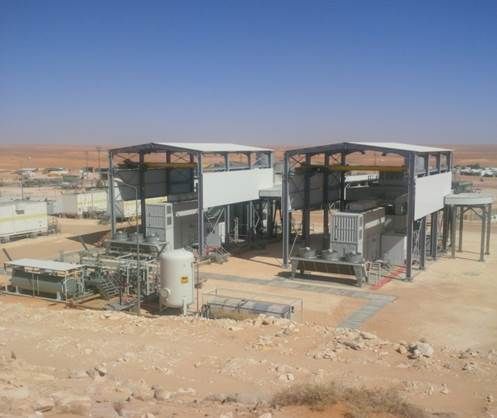 Deux bâtiments industriels sur pilotis dans un environnement désertique, avec machines et équipements à l'extérieur.