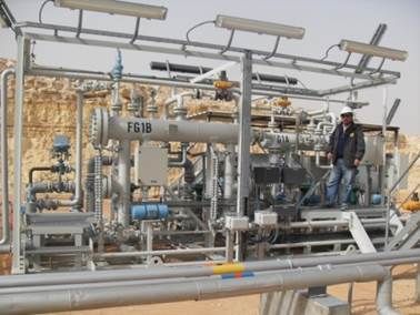 Un homme debout près d'un équipement industriel dans un champ pétrolifère du désert.